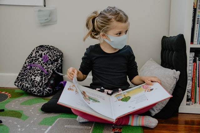 Young child wearing a mask and reading a book at a literary nonprofit organization