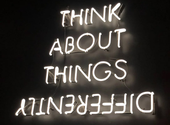 A neon sign saying “Think about things differently” in capital letters with the word “differently upside-down.