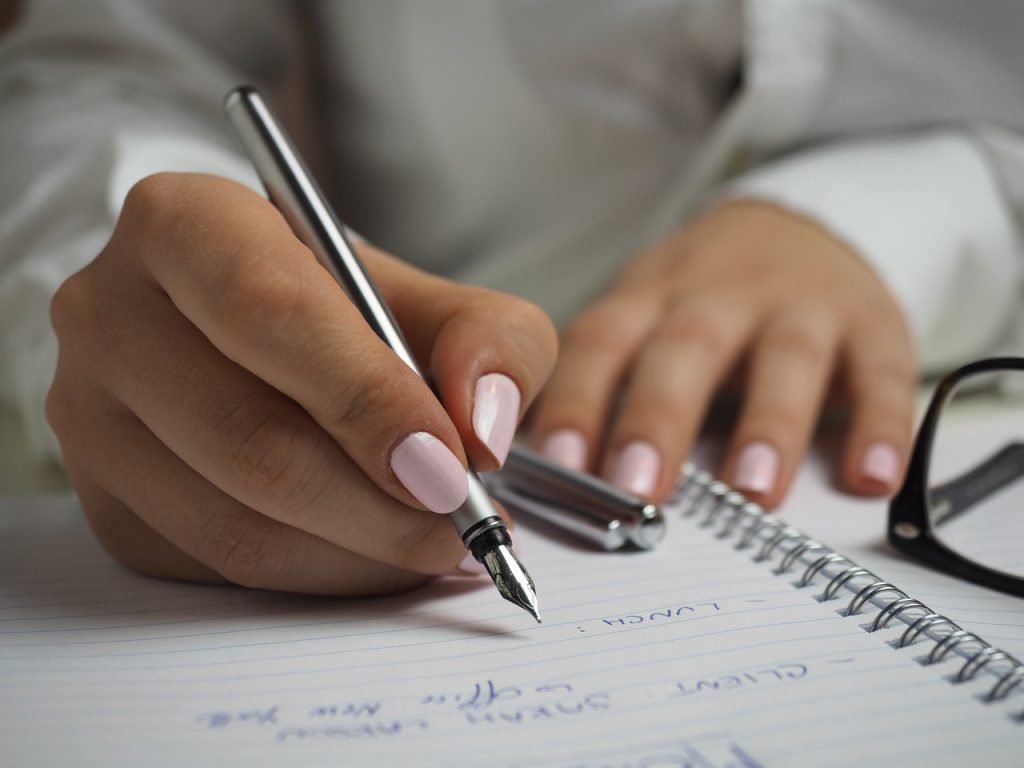 A woman’s hands are seen writing in a notebook.