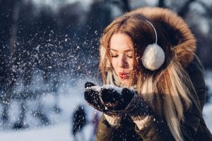 A woman in earmuffs blows into a scoop of fresh snow on her mittens