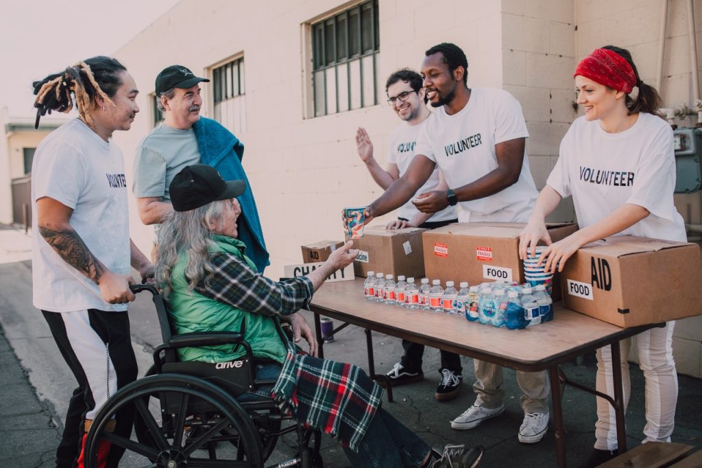 Volunteer giving food to a differently-abled elderly man in wheelchair