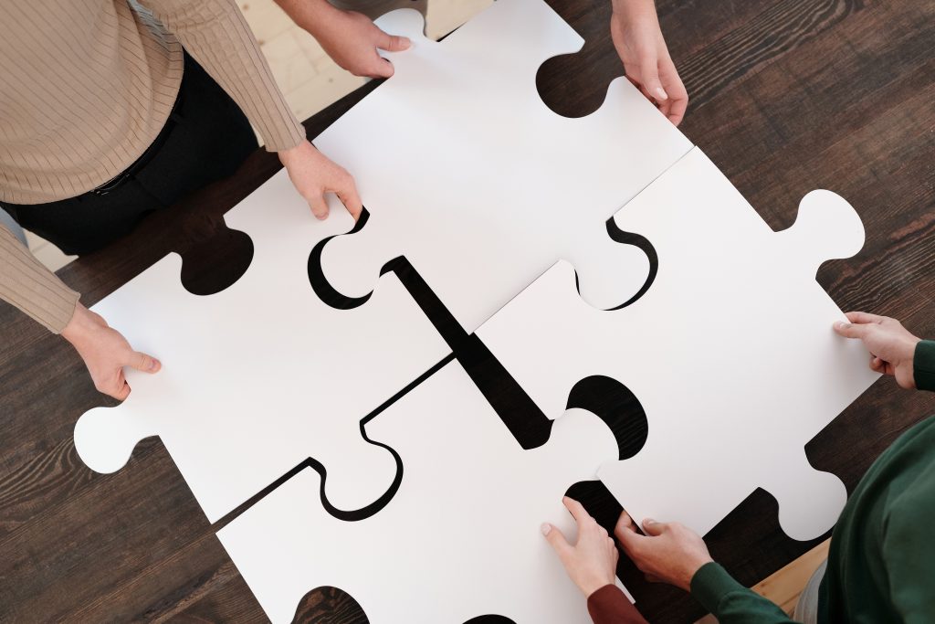 Four people arranging white puzzle pieces on table